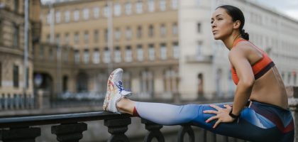 Woman stretching outdoors on urban street railing in activewear, promoting fitness.