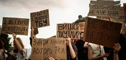 Protesters hold signs with handwritten messages against a cloudy sky.
